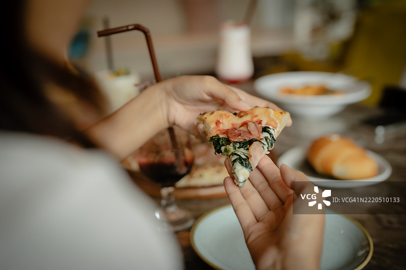 从木桌上一个满盒披萨中伸手拿一片披萨的肩膀视角图片素材