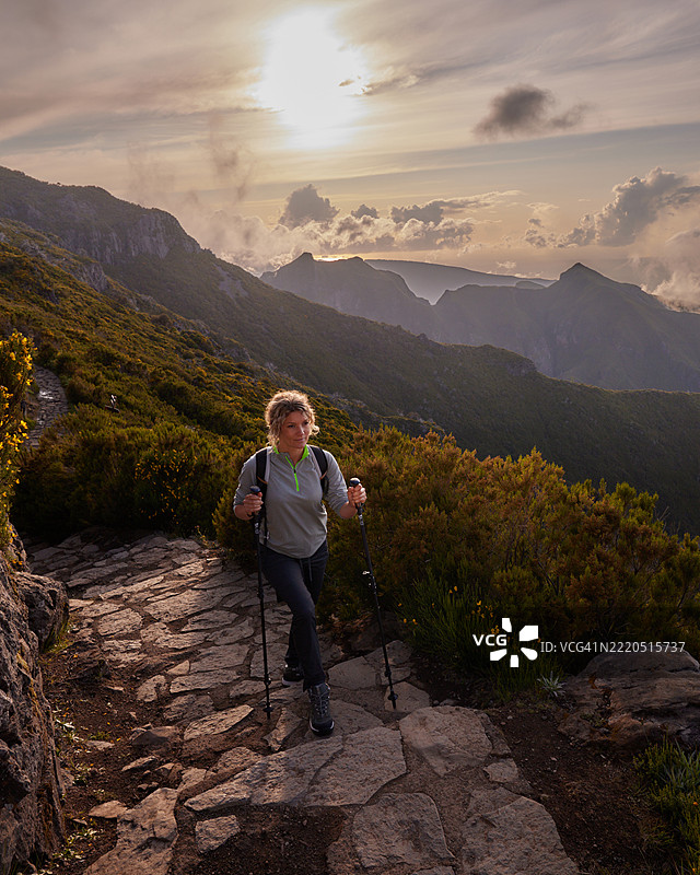 微笑的女性背包客在日落时分徒步登山。图片素材