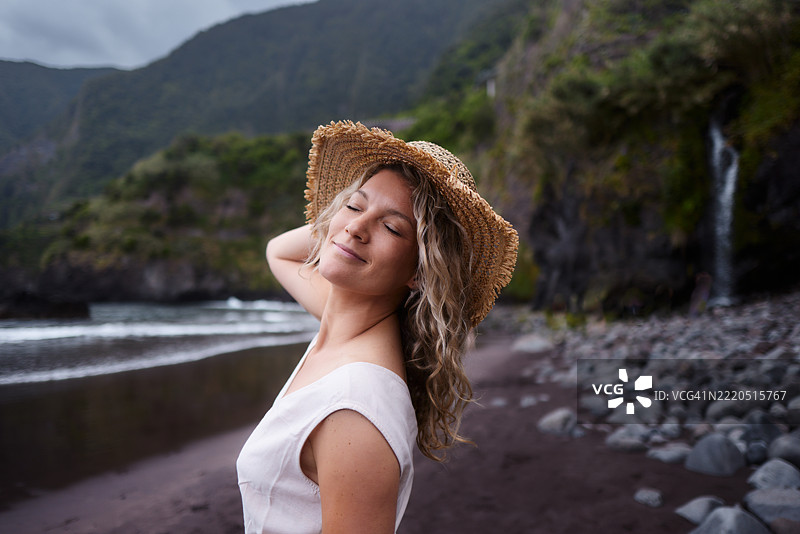 戴着帽子的微笑女性在海滩上享受时光。图片素材