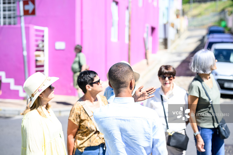 导游从后方带领一群人经过鲜艳的粉色建筑图片素材