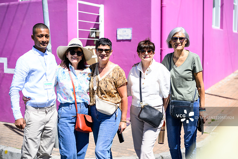 一群微笑的成熟游客在博卡普的热闹街道上合影留念，参加步行游。图片素材