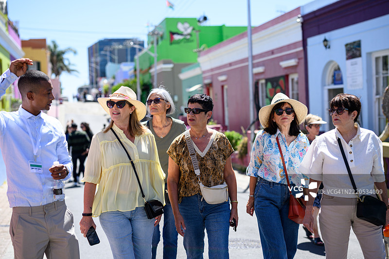 成熟的女性游客在老城区与导游一起沿着色彩斑斓的街道漫步图片素材