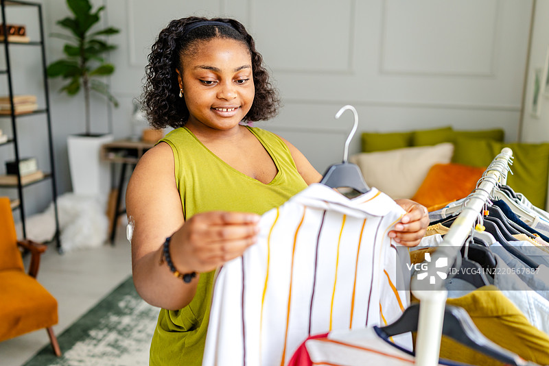 年轻女性在时尚卧室的下午享受挑选衣服的乐趣，患有1型糖尿病。图片素材