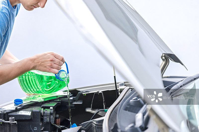 在引擎舱中为汽车冷却系统加注液体的人图片素材