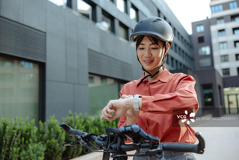 年轻女性在户外骑自行车时查看智能手表，佩戴着头盔图片素材