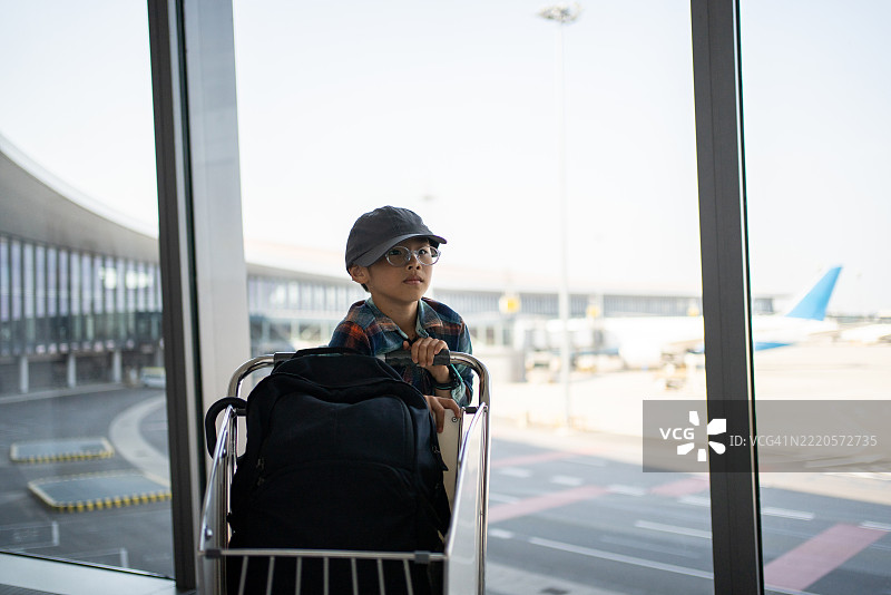 一个亚洲男孩在机场候机厅推着行李推车图片素材
