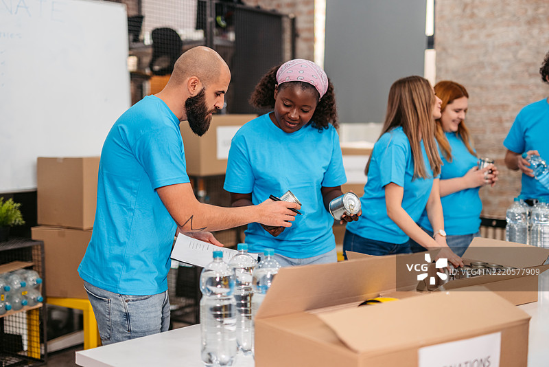 志愿者在捐赠中心将水瓶和食品罐装入捐赠箱中图片素材