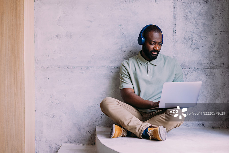 男子坐在室内，使用笔记本电脑并戴着耳机工作图片素材