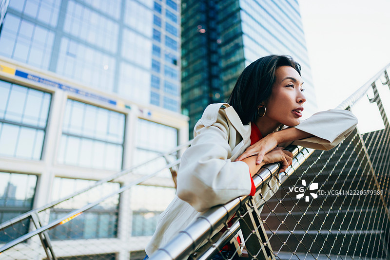 沉思的女性倚靠在现代城市建筑环境中的栅栏上图片素材