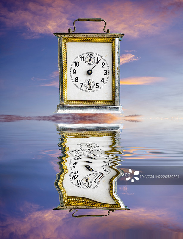 一只旧闹钟在日落时分的水面上倒影。图片素材