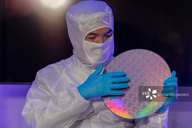 电子制造厂的半导体生产。工人或工程师穿着医疗防护服或白色工作服，手持硅晶圆。图片素材