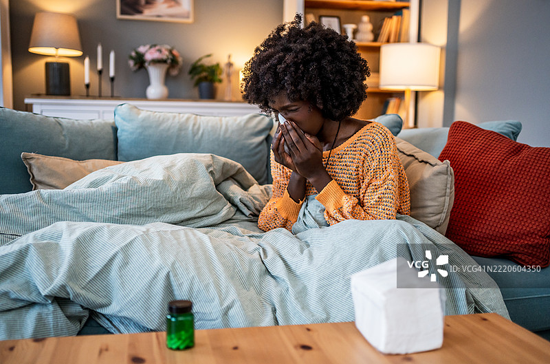 生病的年轻女性在家里的沙发上擤鼻子图片素材