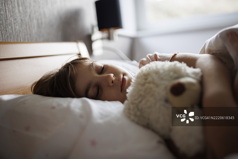 可爱的小女孩抱着她的泰迪熊睡觉图片素材