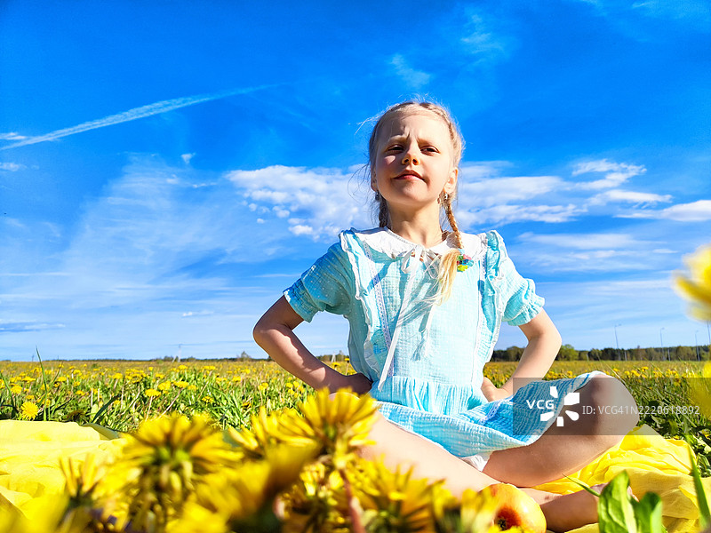 一个女孩自信地坐在蓝天下的明亮蒲公英田野中图片素材
