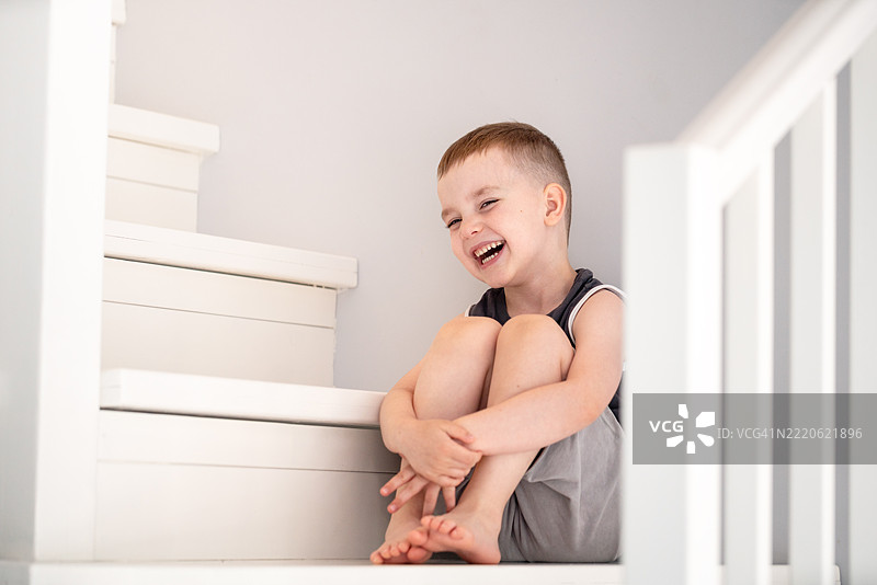 微笑的年轻男孩坐在楼梯上，享受快乐和放松的时刻图片素材