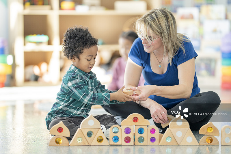 老师在托儿所学习环境中帮助孩子玩玩具图片素材