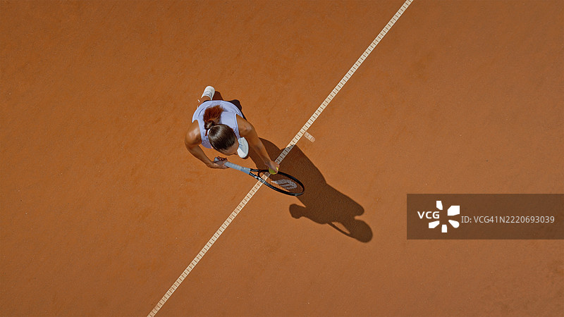 专注的女性网球运动员在阳光明媚的红土场上发球图片素材