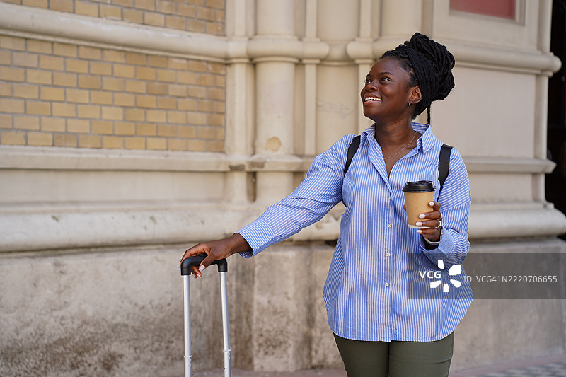 年轻的黑人女性旅行者在欧洲城市探索，手里拿着行李箱、咖啡杯和地图。城市旅游概念，展现了一位自信的女性在旅途中导航并享受旅程。图片素材