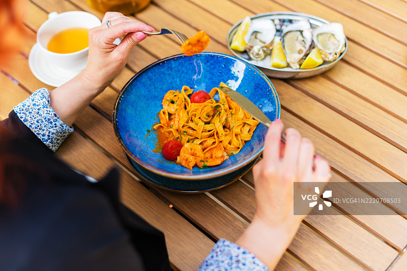 女人手持叉子，叉着番茄虾仁意大利面特写图片素材