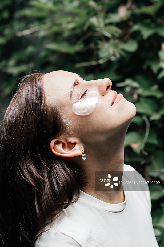女人在大自然中享受宁静，闭着眼睛，眼下贴着闪亮的水凝胶眼贴。一个平和的户外自我护理和护肤时刻。图片素材