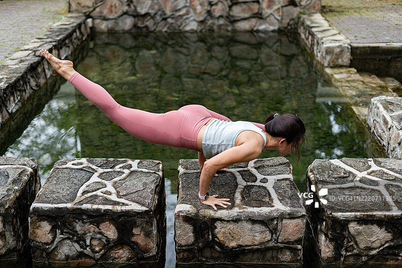 年轻女性在水面上做瑜伽倒立姿势图片素材