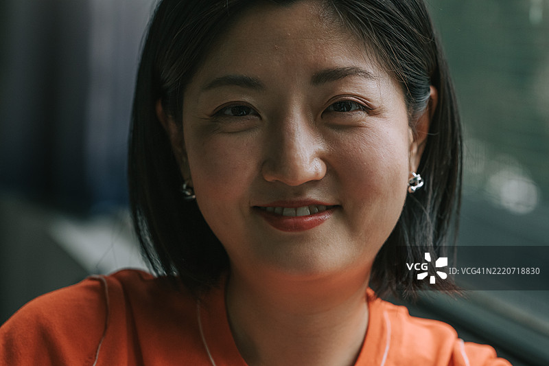 微笑的日本女性在窗边放松，注视着镜头图片素材