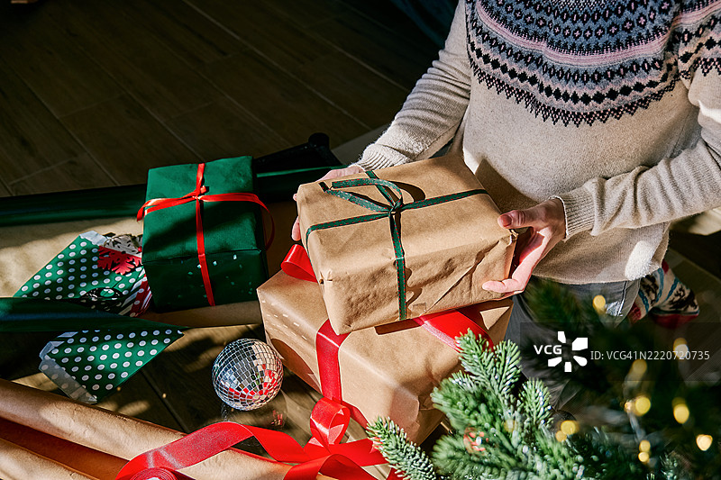 女人在圣诞树旁拿着圣诞礼物盒。冬季节日庆祝活动。图片素材