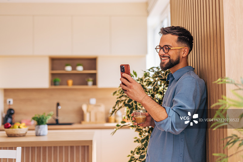 年轻男子在现代厨房享受咖啡休息时间并浏览智能手机图片素材