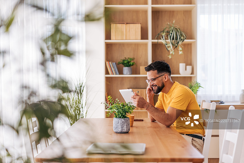 年轻男子在家工作，使用平板电脑并打电话图片素材