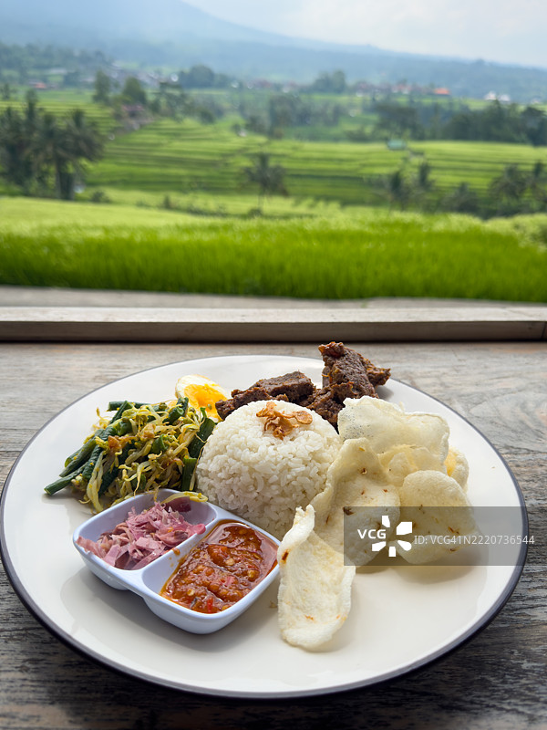 一盘印尼牛肉仁当，背景是稻田梯田的美景图片素材