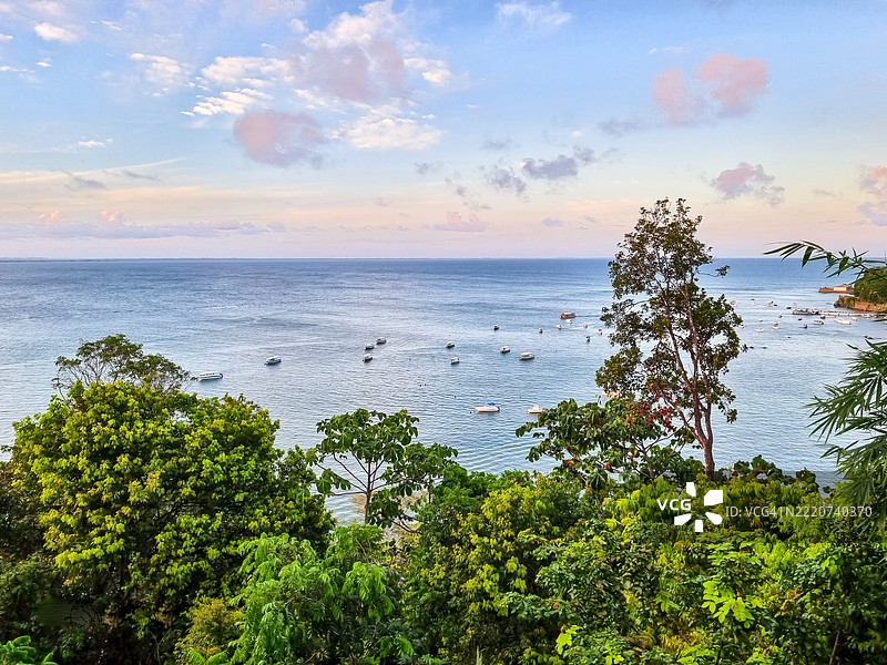 在柔和的天空下，船只静静地停靠在平静的海面上，周围被茂盛的圣保罗山绿植环绕，正值黎明或黄昏时分。图片素材