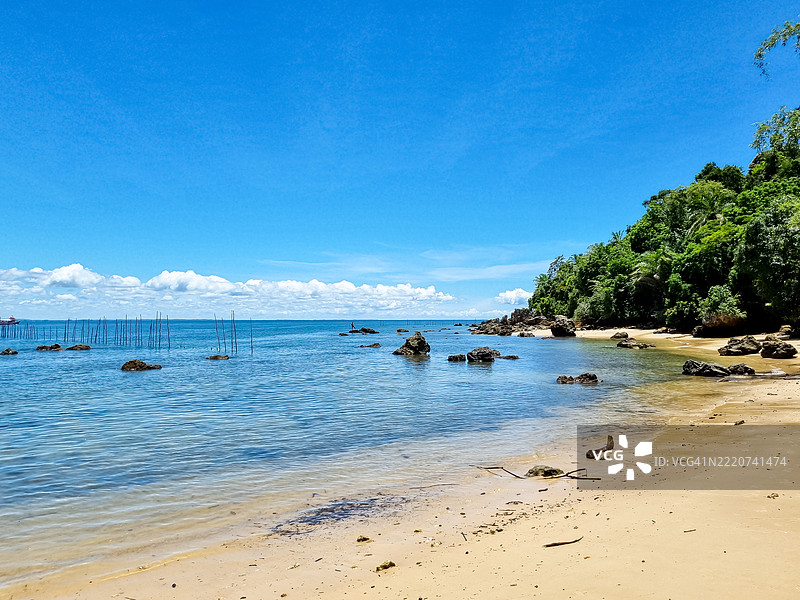 巴西莫罗圣保罗的宁静海岸线：碧蓝的海水、沙滩、岩石点缀、木桩、郁郁葱葱的绿色背景和明亮的蓝天。图片素材