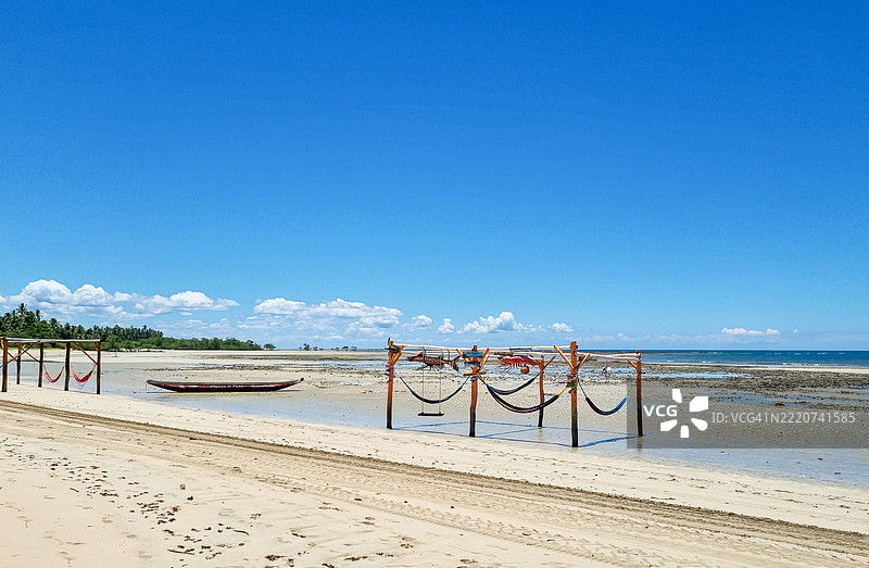 五彩斑斓的吊床在金色沙滩上摇曳，一只孤独的小船静静停靠在温柔的海浪旁，巴西莫罗圣保罗宁静海岸的宁静天空下。图片素材
