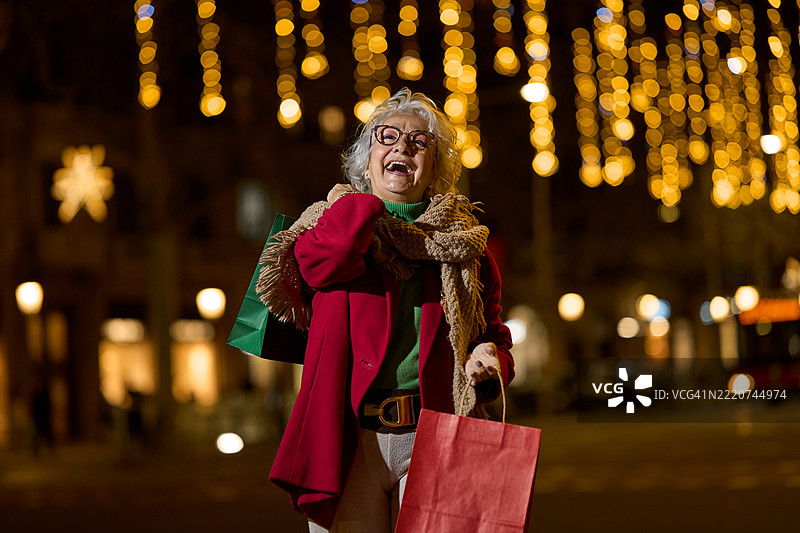 快乐的老年女性在圣诞市场上提着购物袋图片素材