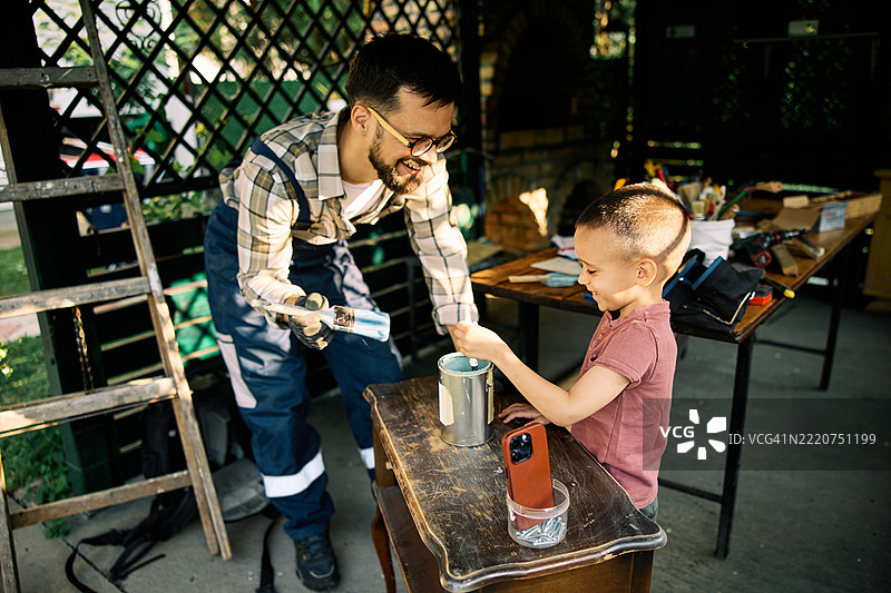 快乐的工匠和他的儿子在工作坊准备为旧家具上漆。图片素材