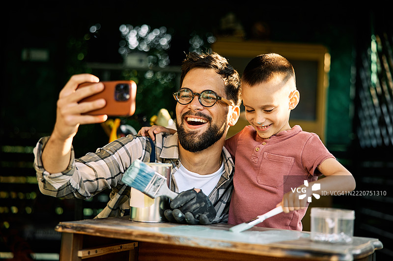 工匠和他的儿子在工作室里给旧家具上色时自拍。图片素材