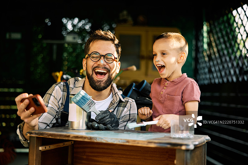 快乐的父亲和儿子在手工艺工作坊里拍自拍，鼻子上涂着颜料。图片素材