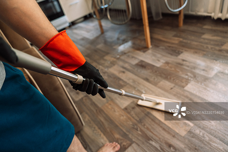 男子戴着手套，手握拖把柄，在现代厨房内清洗地板图片素材
