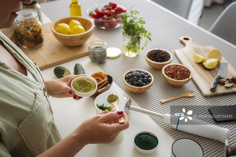 辣木粉和螺旋藻混合饮料，女性正在准备健康的绿色排毒饮品，水果和蔬菜的奶昔，适合健康和减肥计划。厨房和浸入式搅拌机图片素材