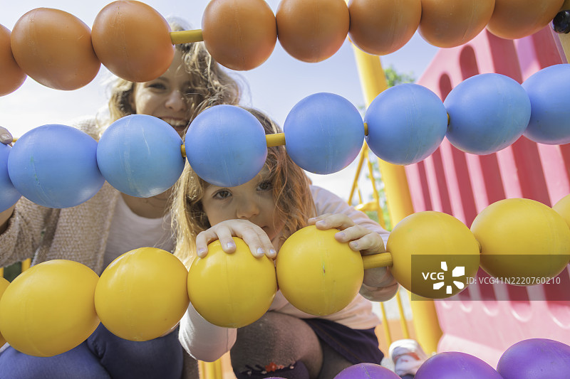 好奇的小女孩和她的母亲在游乐场的结构上玩五彩的算盘珠子图片素材
