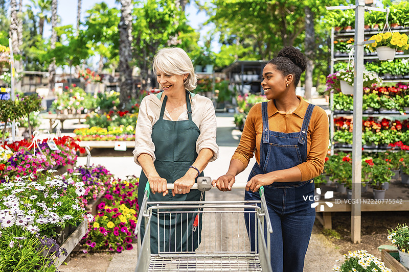 两名女性园艺中心工作人员在五彩缤纷的花盆之间推着一辆空购物车图片素材