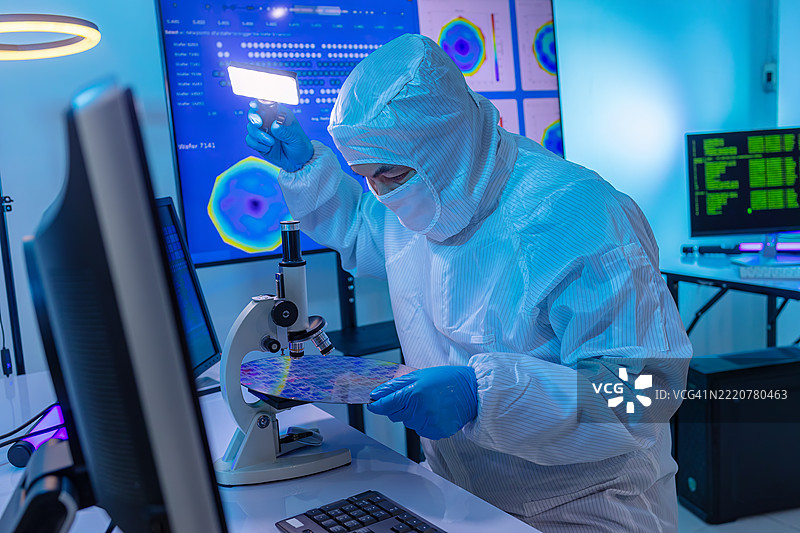 电子制造厂的半导体生产。工人或工程师穿着医疗防护服或白色工作服，手持硅晶圆。图片素材