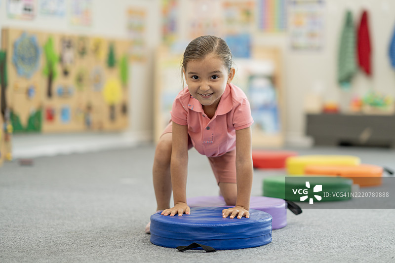 年轻女孩在色彩鲜艳的幼儿园活动室里玩耍，面带微笑。图片素材