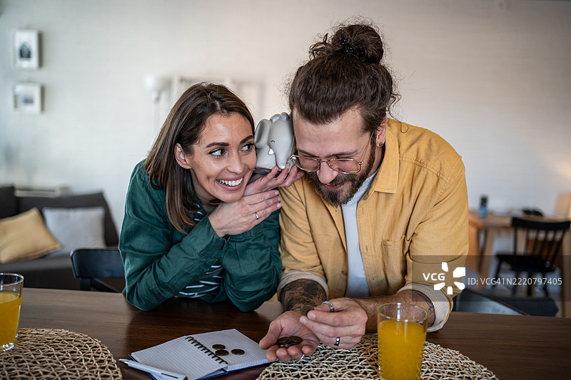 快乐的情侣在家里数硬币并拿着储蓄罐图片素材