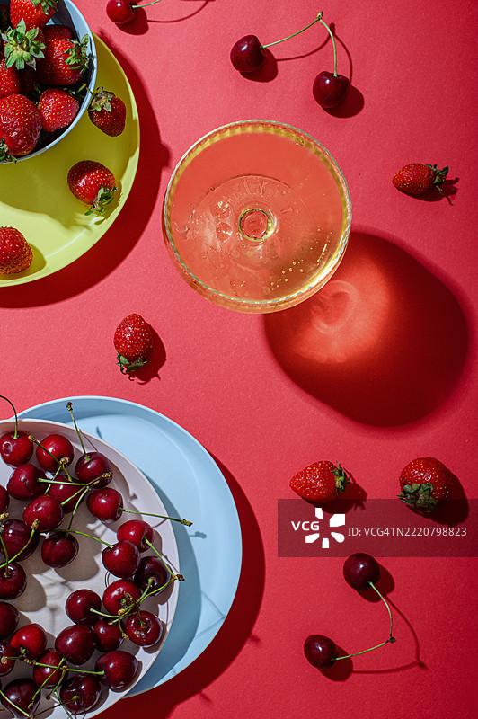 鲜艳的夏季静物画，背景为红色，包含草莓、樱桃和气泡饮料图片素材