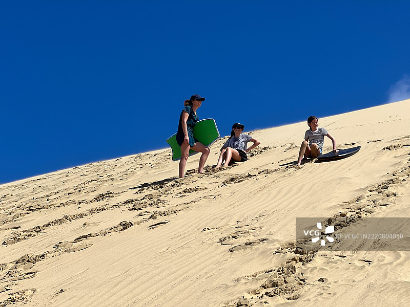 一群游客使用冲浪板从高高的沙丘上滑下。图片素材
