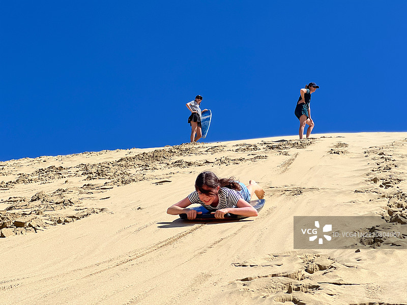 游客在高沙丘上滑行，使用冲浪滑板。图片素材