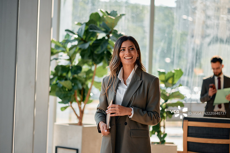 微笑的女商人在现代办公室里走动，手里拿着平板电脑图片素材