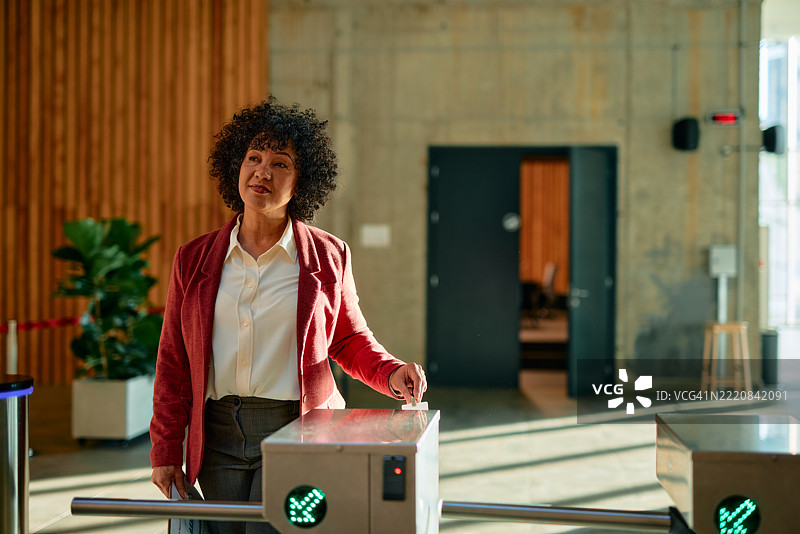 女商人通过电子旋转门进入办公室，使用门禁控制系统。图片素材