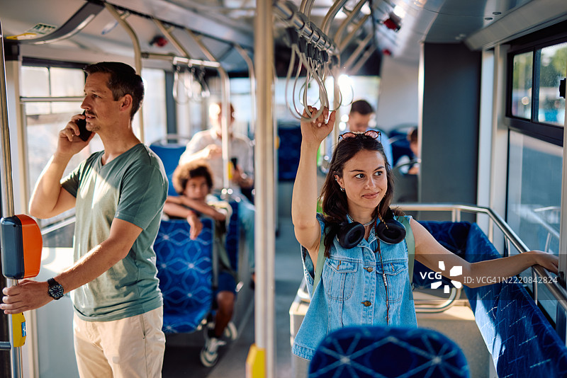 年轻女性在公交车上通勤，握着扶手，望向窗外。图片素材